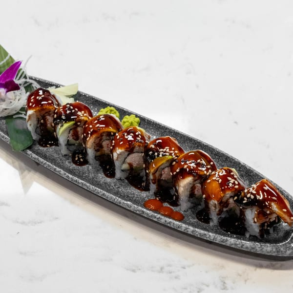A long plate of sushi rolls with eel, avocado, and sesame seeds, drizzled with sweet sauce.