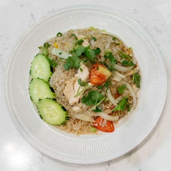 Chicken fried rice with sliced cucumbers, tomatoes, onions, and cilantro on a white plate.