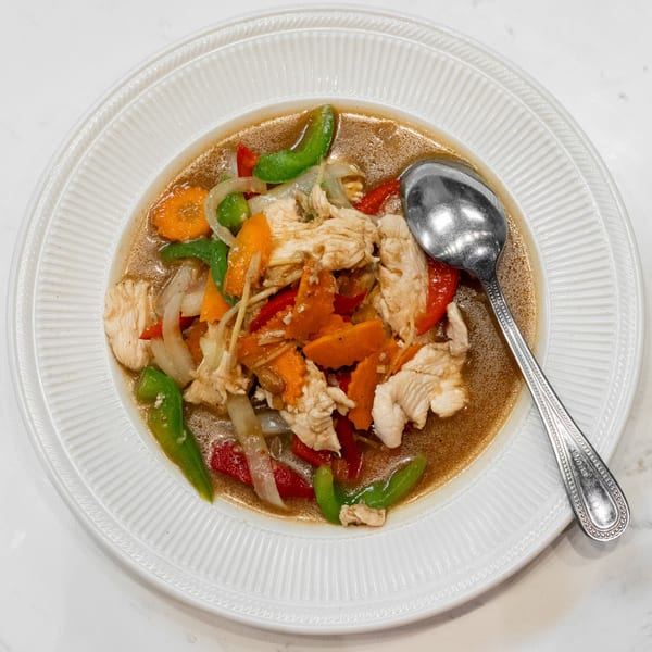 A white plate of chicken stir-fry with carrots, bell peppers, and onions in a savory sauce.