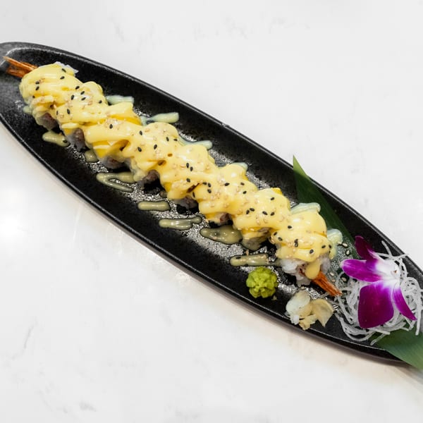 Sushi roll topped with yellow sauce and black sesame seeds, garnished with a purple orchid.