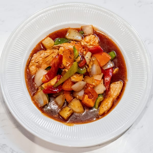 Sweet and sour chicken with bell peppers, onions, and pineapple in a white bowl.
